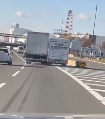 Auto a nákladné auto na ceste, v pozadí ruské koleso a moderné budovy na slnečný deň.