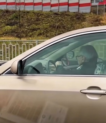 Starší vodič za volantom osobného auta na ceste, pozadie tvorí plot a plotný panel.