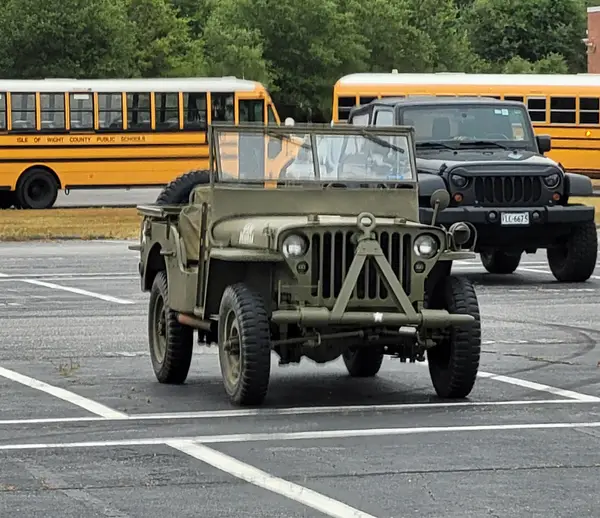 Historické vojenské vozidlo Jeep parkuje vedľa školských autobusov na parkovisku.