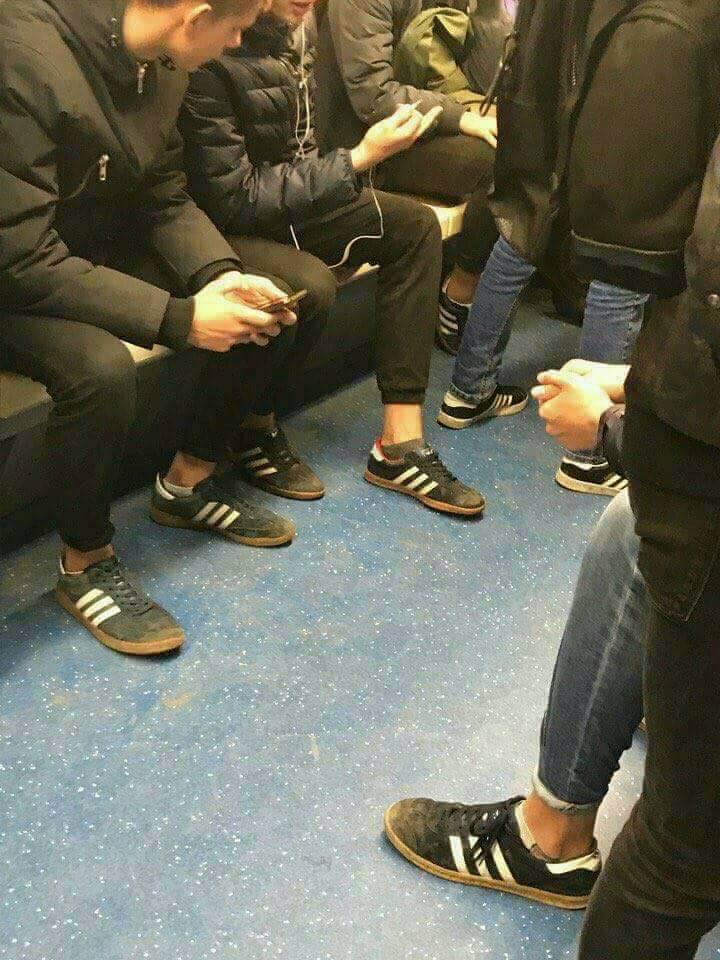 Skupina ľudí sedí v metre, všetci v obuvi s tromi pruhmi, modrý podlahový interiér.