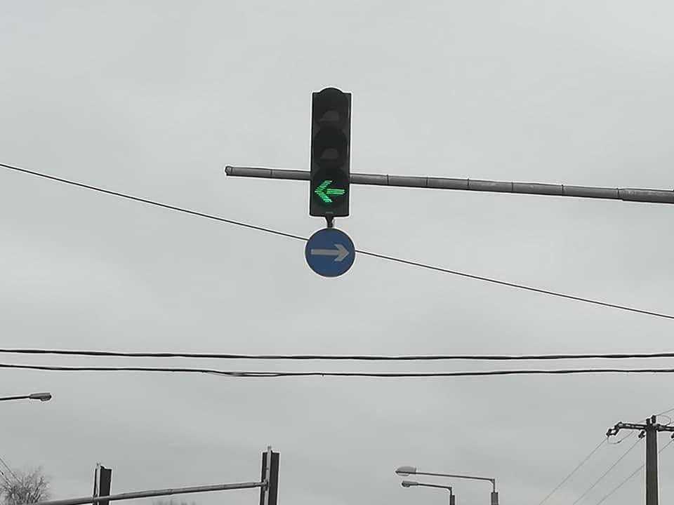 Dopravný semafor so zelenou šípkou doľava, dopravná značka ukazuje smer doprava, oblačná obloha.