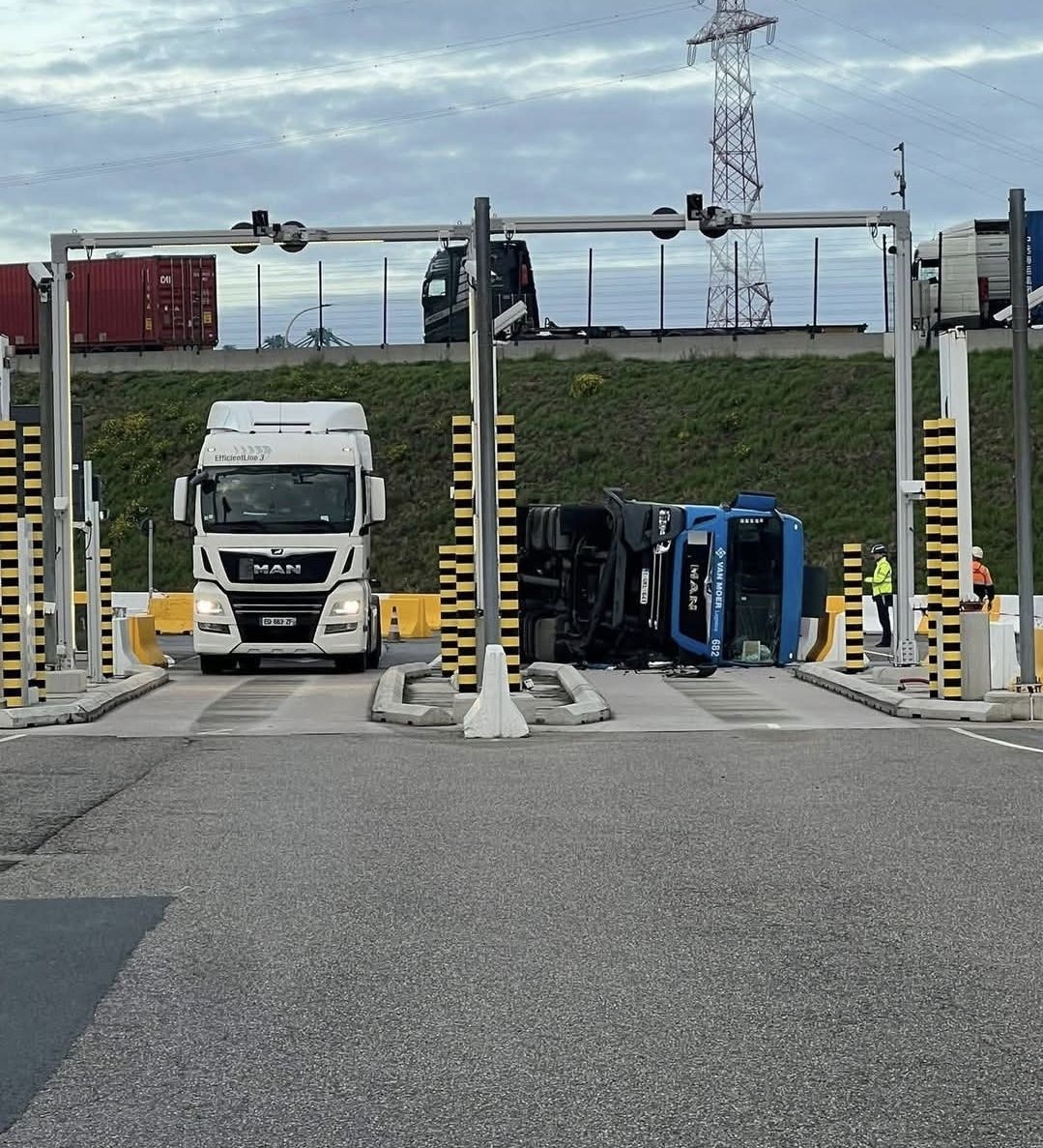 Kamión prevrátený na bočnej ceste pri mýtnej bráne, okolo prechádza biely kamión MAN.