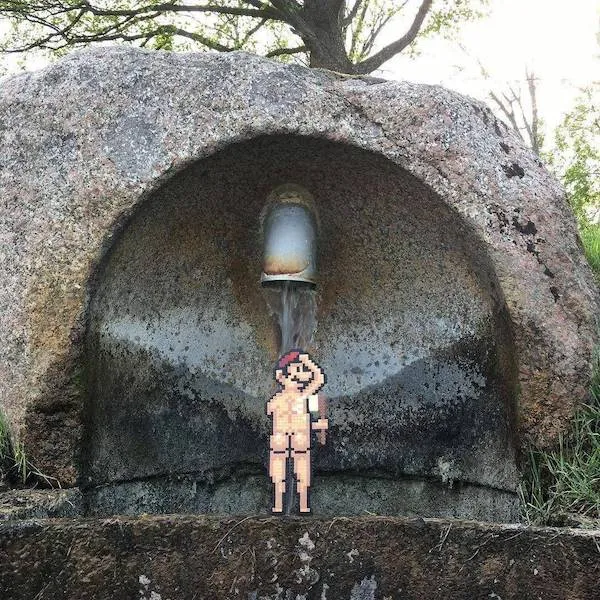 Pixelová postavička pod fontánou v skale, pripomínajúca umenie v prírode.