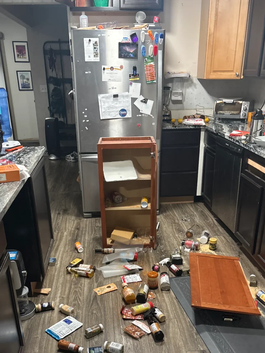 Rozbitá kuchynská skrinka, korenie a jedlo rozhádzané po podlahe v kuchyni. Nečakaný chaos v domácnosti.