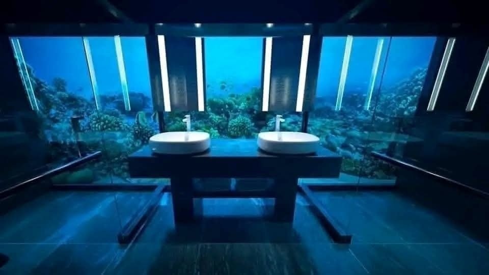 Moderná kúpeľňa s dvomi umývadlami a výhľadom na podmorský svet cez sklenenú stenu.