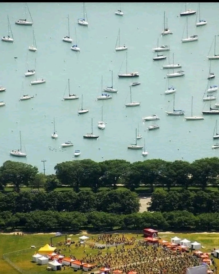 Lode plávajúce na modrej vode, parkom a zhromaždením ľudí v popredí, pohľad z výšky.