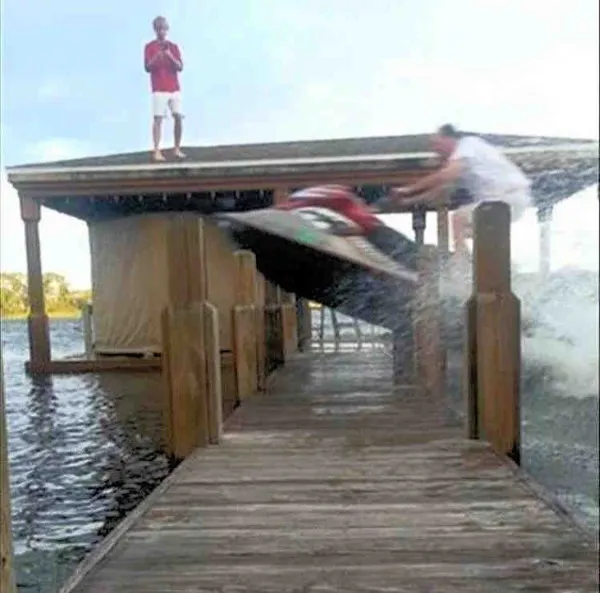 Osoba na vodnom skútri skáče cez mólo, zatiaľ čo divák na streche sleduje odvážny kúsok.