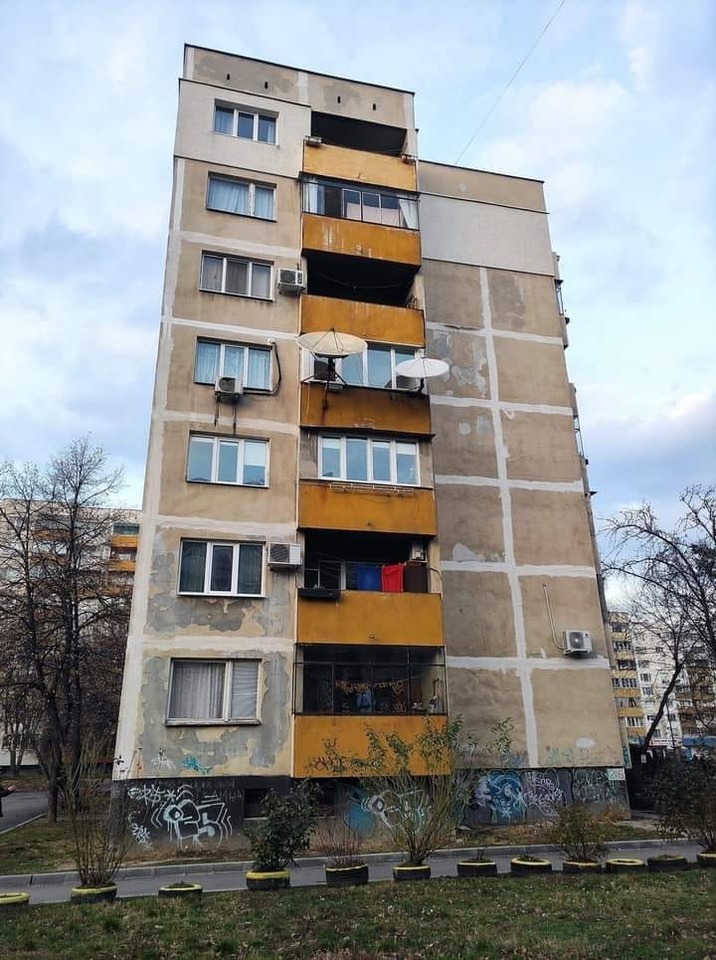 Opustený bytový dom so zašlými fasádami, satelitnými anténami a grafitmi na prízemí.