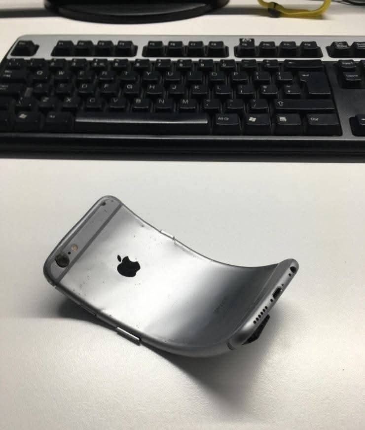 Zahnutý iPhone na stole pred klávesnicou, ilustrácia problému ohýbania mobilných telefónov.