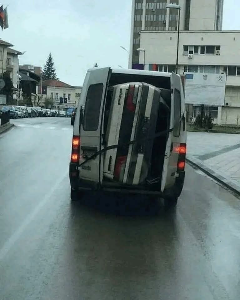 Dodávka s otvorenými dverami prevážajúca auto priviazané popruhmi v meste na daždivom dni.