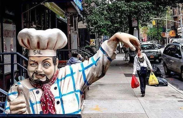 Socha kuchára s vysokým klobúkom vedľa ulice, žena kráča s nákupnými taškami v New Yorku.