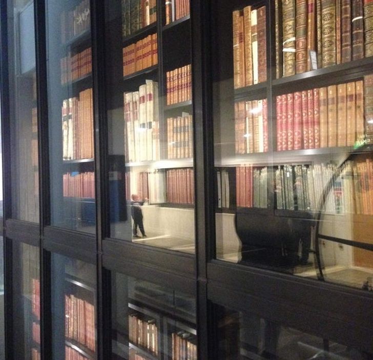 Reflexia v zasklenej knižnici s leštenými policami plnými kníh v historických väzbách.