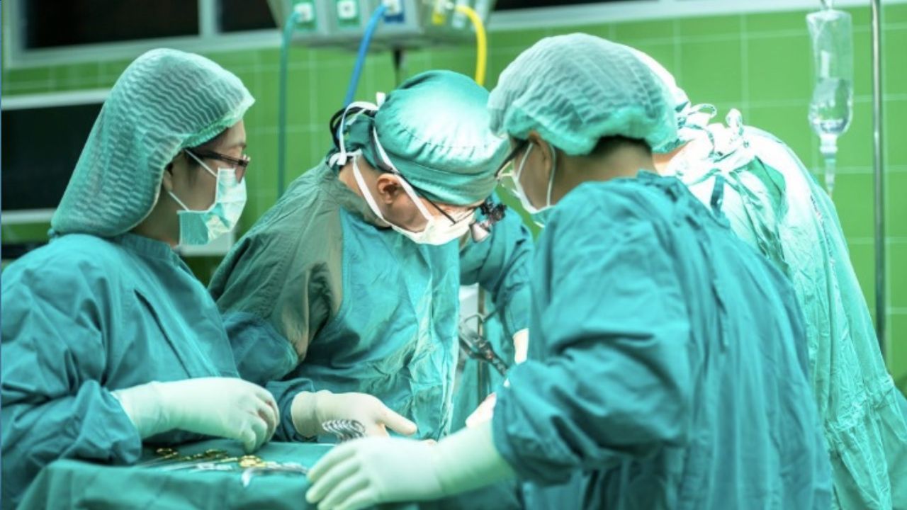 Chirurgický tím operuje v nemocnici, oblečení v sterilných zelených rúchach a maskách, so zaostrením na precíznosť práce.