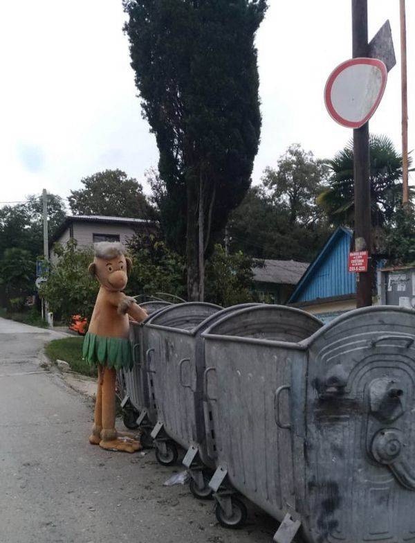 Kostým postavy prezerá kontajnery na odpad na vidieckej ulici.