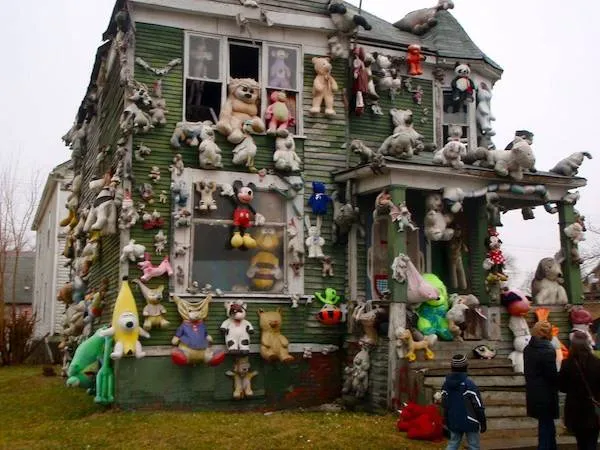 Starý dom pokrytý množstvom plyšových hračiek rôznych druhov a veľkostí, pozorovaný okoloidúcimi ľuďmi.