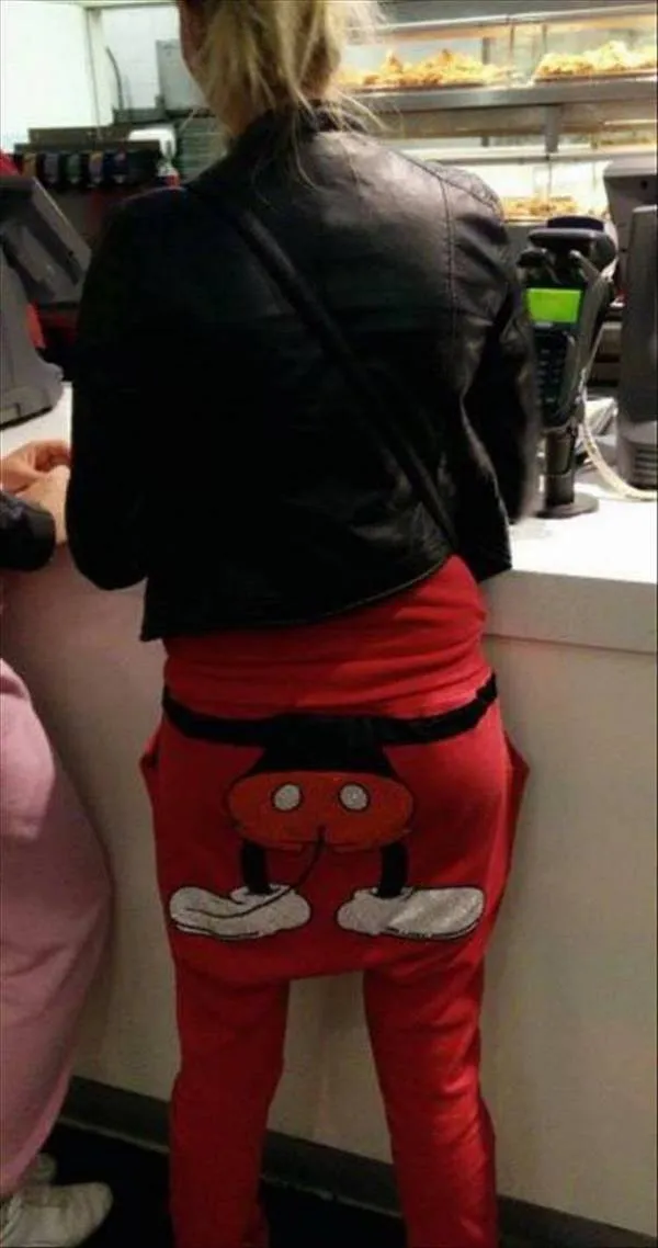 Osoba v čiernej bunde a červených nohaviciach s kresleným motívom čaká v rade pri pulte.