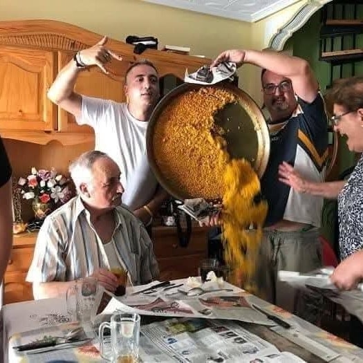 Rodinný obed: dva muži náhodne preklápajú veľký hrniec s ryžovým jedlom nad stolom.