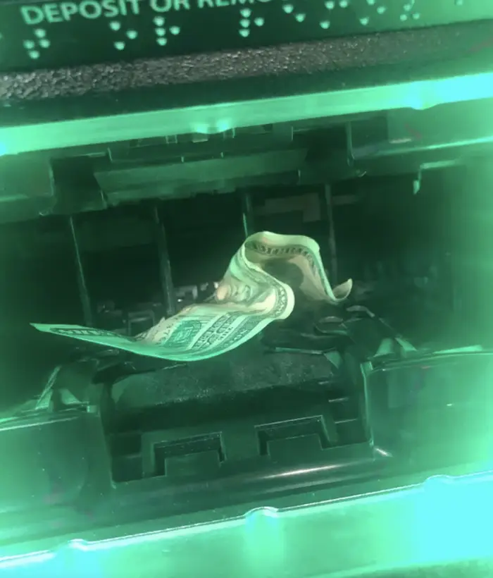 Štyri bankovky uviazli v bankomate, jasné zelené svetlo osvetľuje výdajný otvor automatu.
