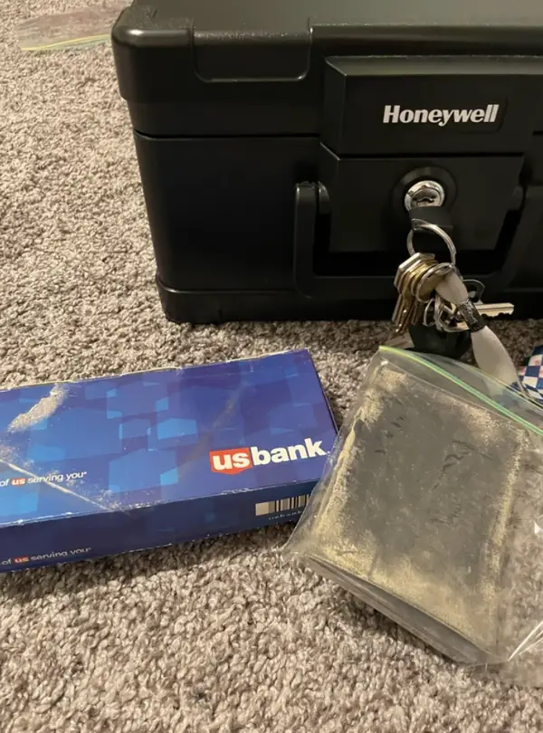 Bezpečnostná schránka s kľúčmi, banková obálka a čierna taška na koberci.
