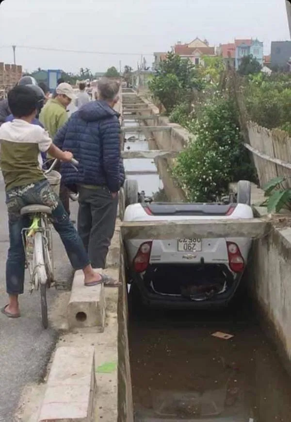 Auto prevrátene v priekopovom kanále, okolo stoja zvedaví ľudia na bicykloch.