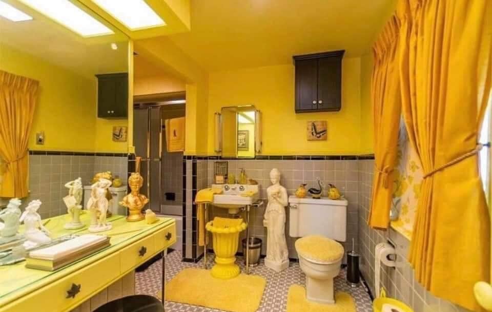 Žlto-sivá retro kúpeľňa so sochami a žltými závesmi, doplnky v odvážnom štýle spojené s vintage eleganciou.