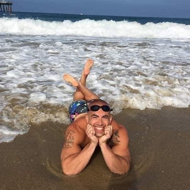 Muž relaxuje na pláži, leží bruškom dole pri oceánskej vode s úsmevom na tvári.