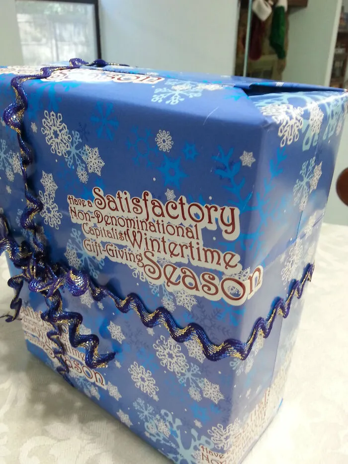 Modrý darčekový obal s vločkami a vtipným textom na tému zimného sviatočného darovania.