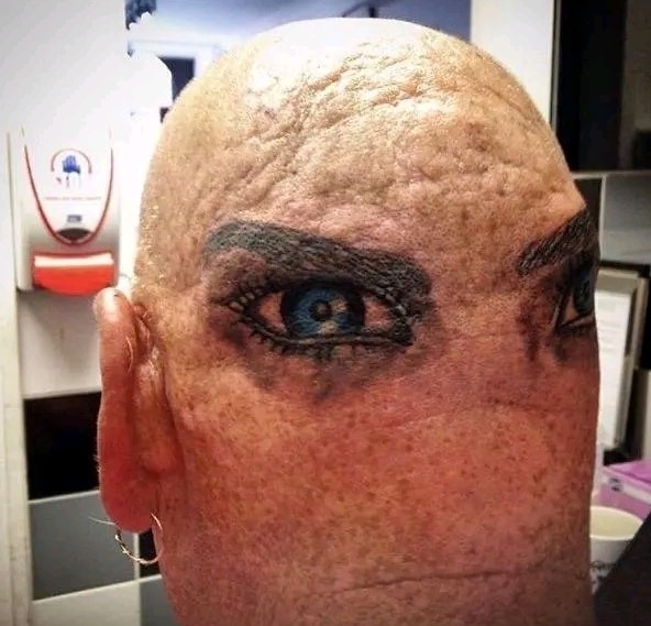 Holá hlava s realistickým tetovaním očí na zadnej strane, iluzívny a nezvyčajný umelecký dizajn.