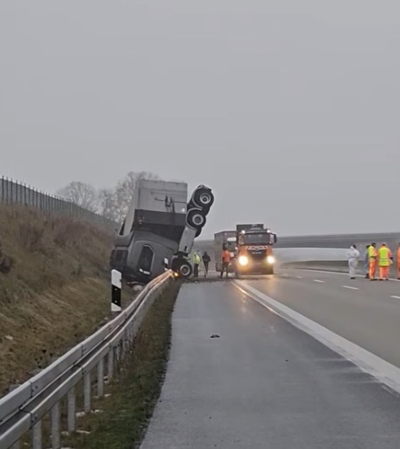 Nákladné auto vychýlené z cesty na diaľnici, pri ňom záchranné tímy. Nehoda pod zamračenou oblohou.