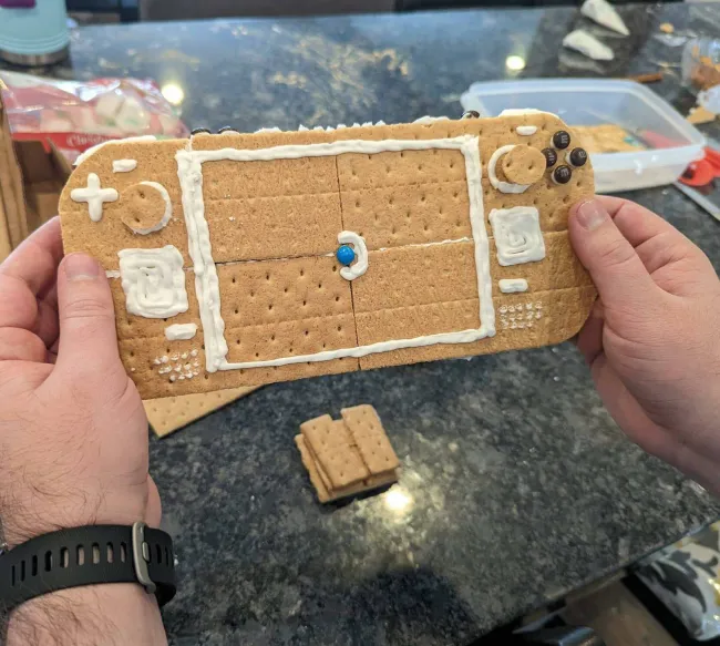 Herný ovládač z krekrov a polevy, ruky ho držia nad kuchynským stolom.