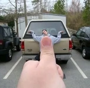 Perspektívna ilúzia: Palec vyzerá, akoby tlačil osobu o auto na parkovisku.