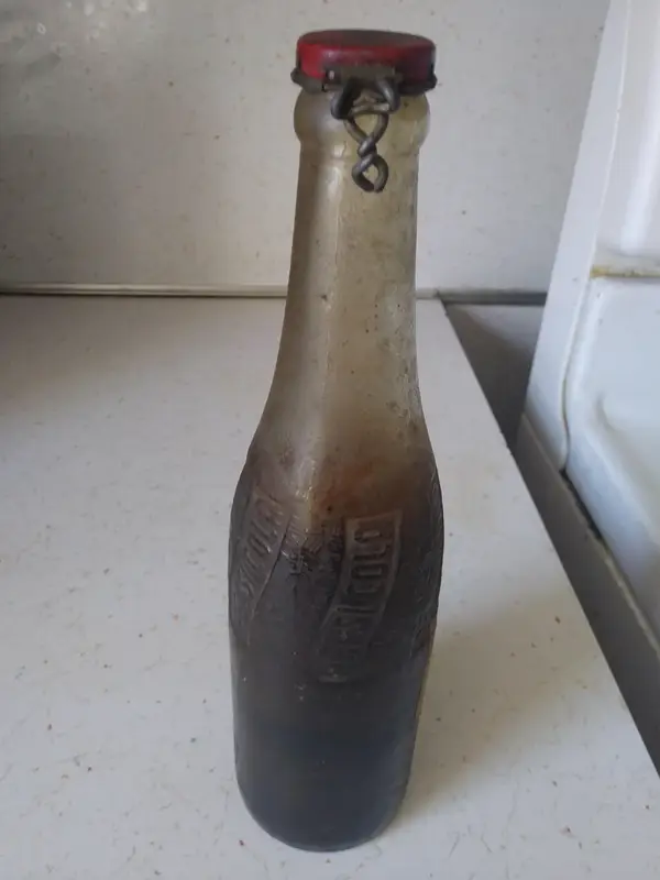 Stará zapečatená fľaša s vrchnákom, stojaca na bielej kuchynskej linke.