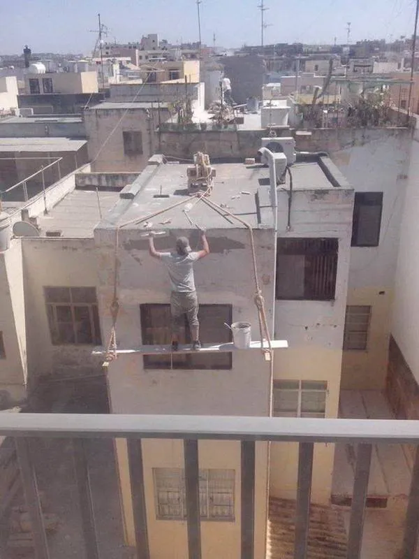 Pracovník na nebezpečnom lešení natiera fasádu budovy vo výške bez bezpečnostných opatrení.