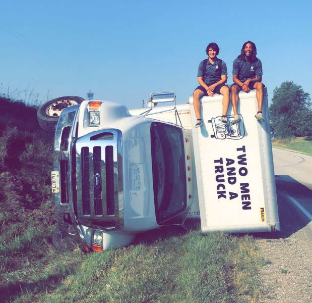 Dva muži sedia na prevrátenom nákladnom aute Two Men and a Truck pri ceste.