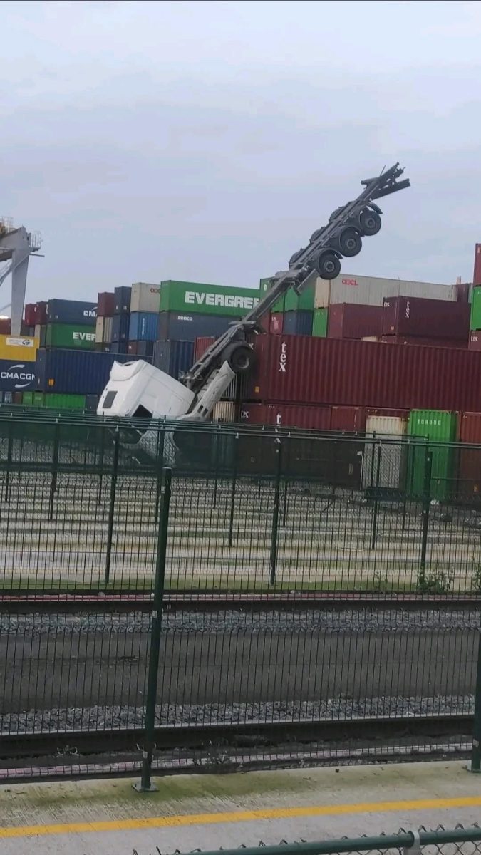 Kamión s návesom prevrátený na niekoľko kontajnerov v prístave, s pneumatikami smerujúcimi nahor.