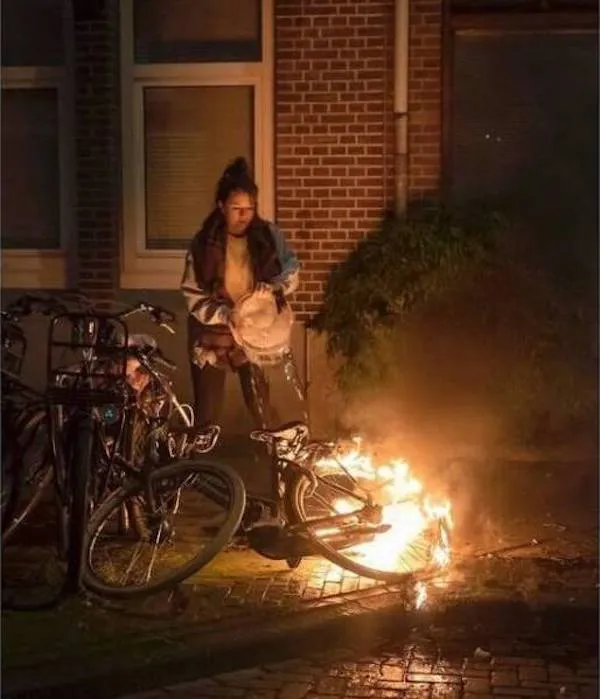 Osoba hasí horiaci bicykel na ulici v noci, zatiaľ čo okolo stoja ďalšie bicykle.