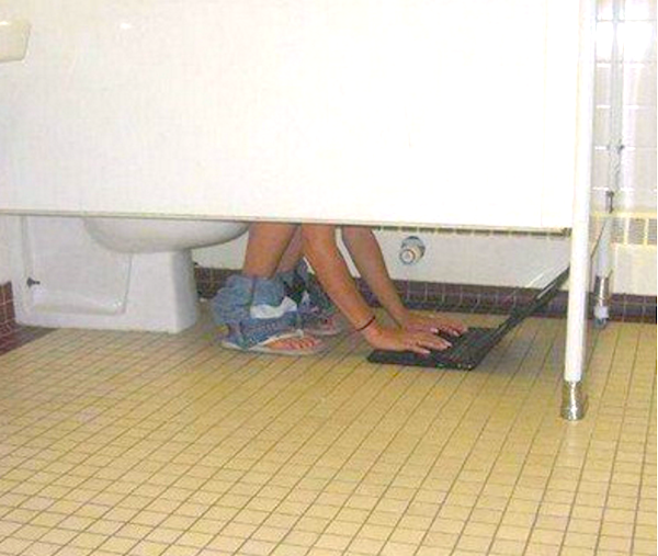 Osoba píše na notebooku na záchode, nohavice dolu, dlaždicová podlaha.