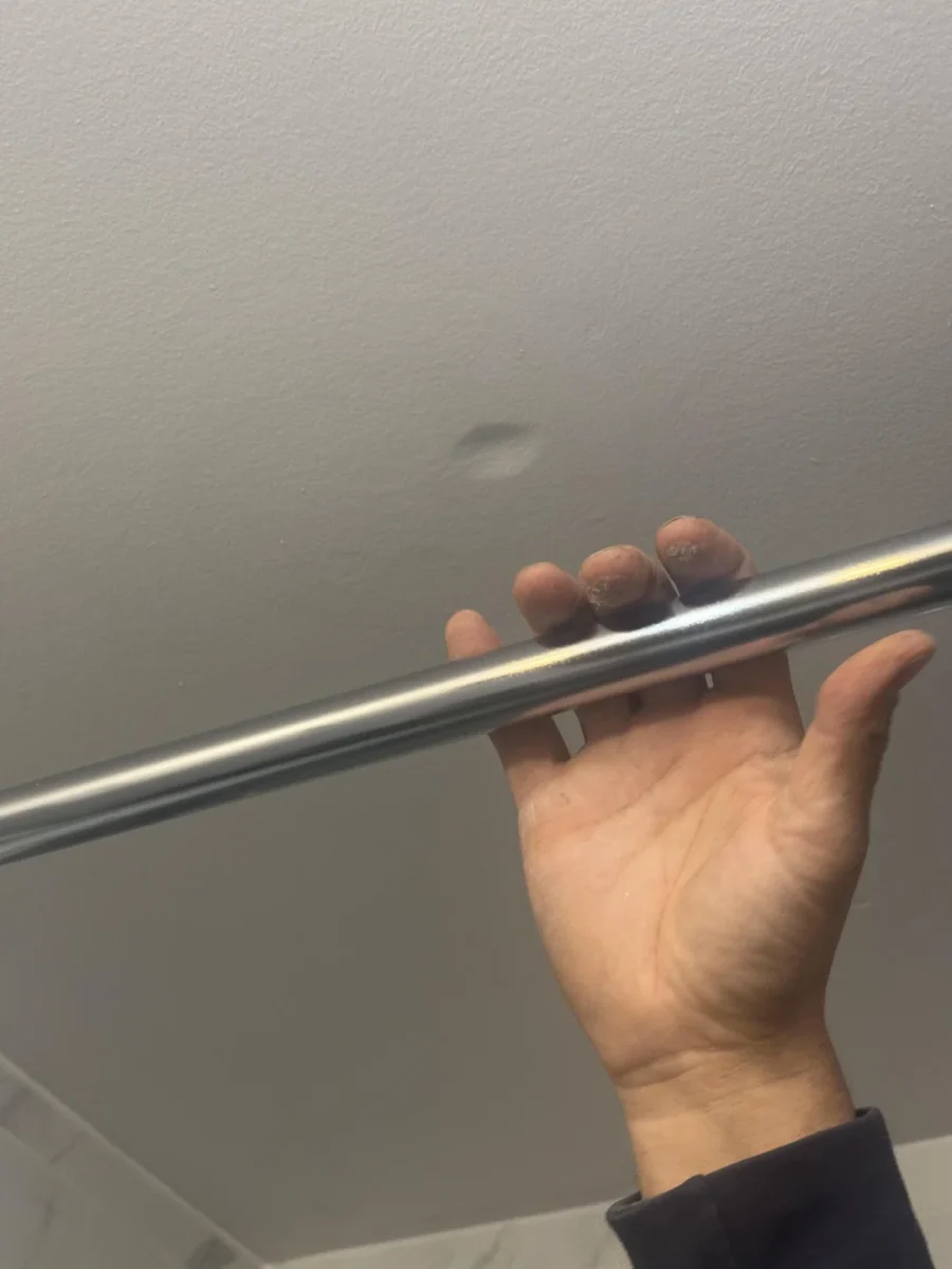 Ruka držiaca kovovú tyč na pozadí bieleho stropu.