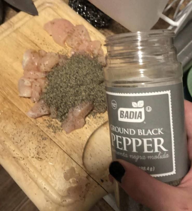 Koreniaca zmes na kuracích kúskach, mletý čierny korenie značky Badia na drevenej doske.