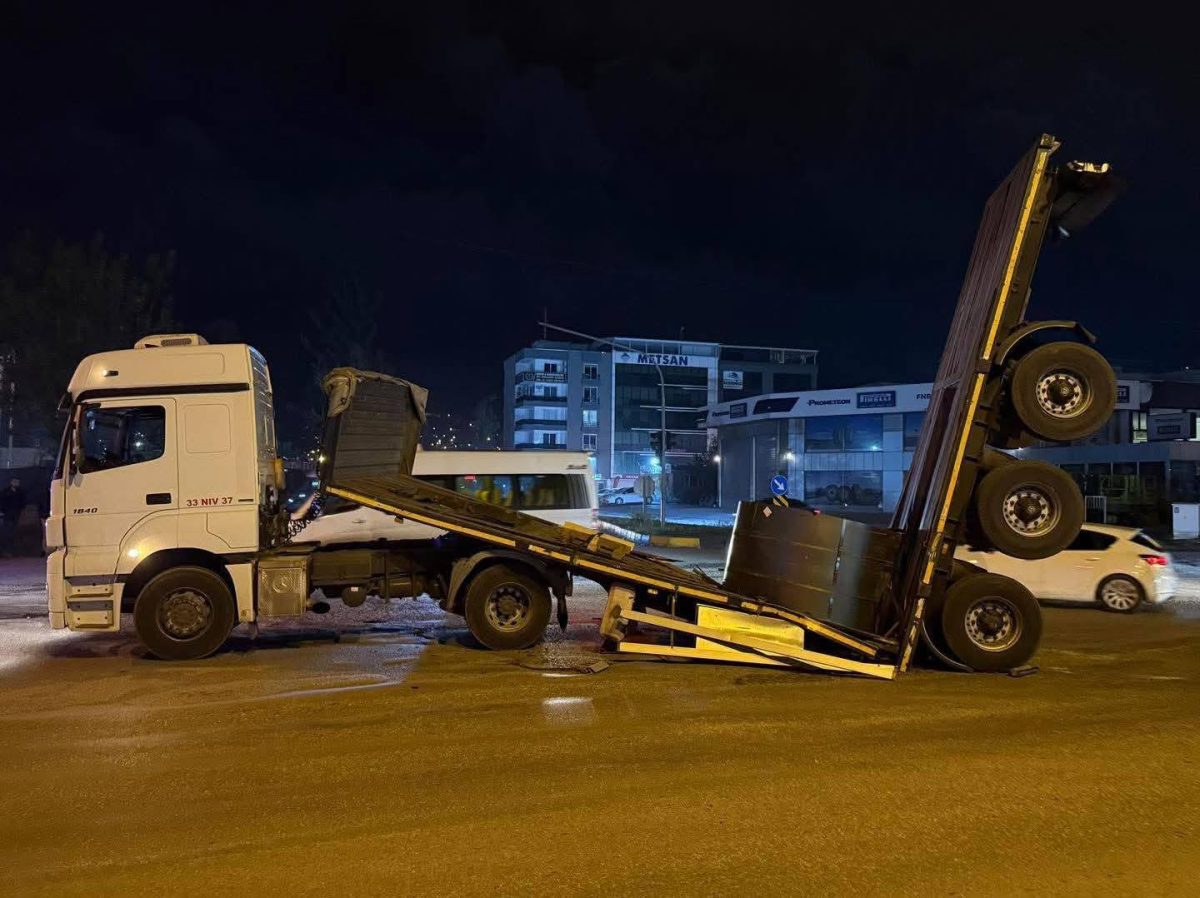 Nákladné auto so zdvihnutou kabínou a prívesom v neočakávanej pozícii na nočnej ulici.