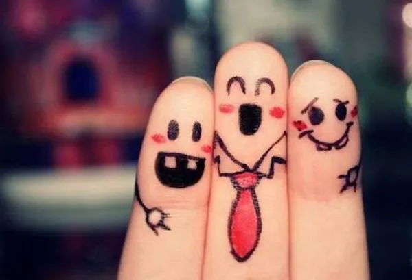 Prsty s nakreslenými usmiatymi tvárami a kravatou, symbolizujúce priateľstvo a zábavu.