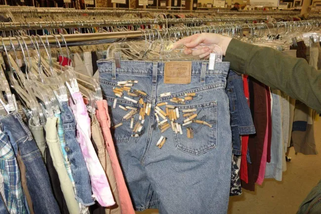 Džínsy s ozdobnými štipcami v stojane s oblečením v second hand obchode, zblízka.