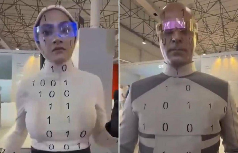 Dva futuristické robotické obleky s binárnym kódom a farebnými okuliarmi na technologickej výstave.