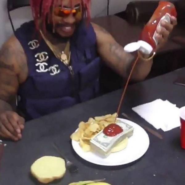 Osoba s červenými vlasmi leje kečup na tanier s čipsami a balíkom bankoviek, sedí pri stole.