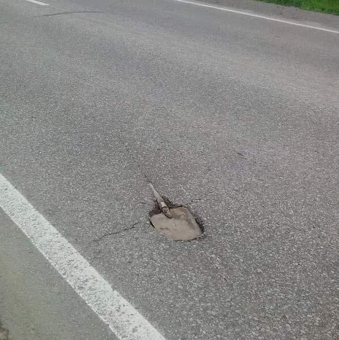 Diera na ceste s lopatou v asfalte, označujúca poškodenie povrchu vozovky.