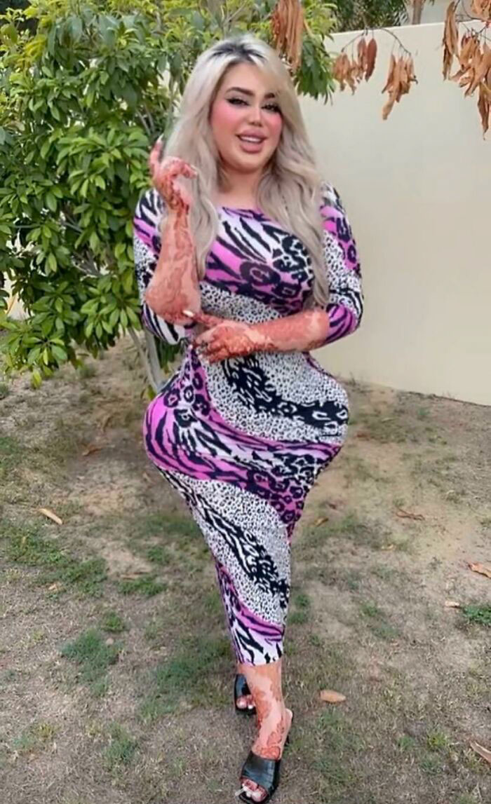 Žena v pestrofarebných šatách a mehndi, stojaca pri stromoch na dvore.