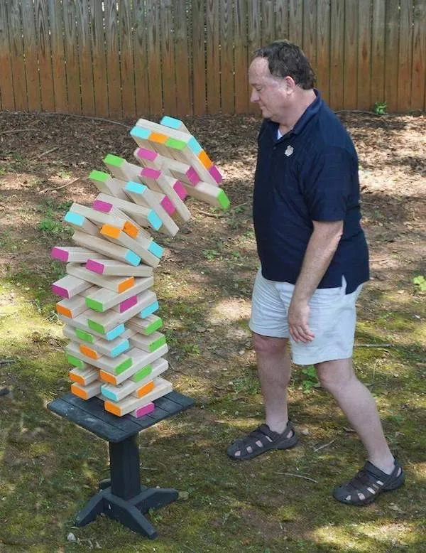 Muž stojaci pri padajúcej veži z farebných drevených blokov vo vonkajšom prostredí.