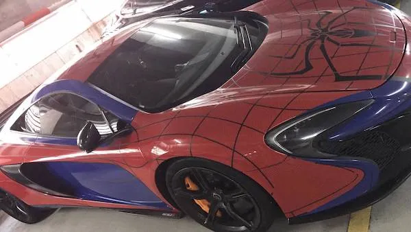 Športové auto s motívom superhrdinu v červeno-modrom prevedení s pavučinovým dizajnom zaparkované v garáži.