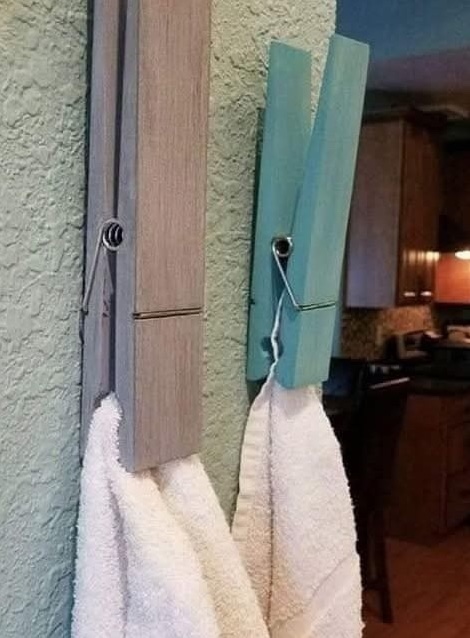 Veľké štipce na prádlo na stene v kúpeľni držia uteráky, originálny a praktický nápad na úložný priestor v domácnosti.