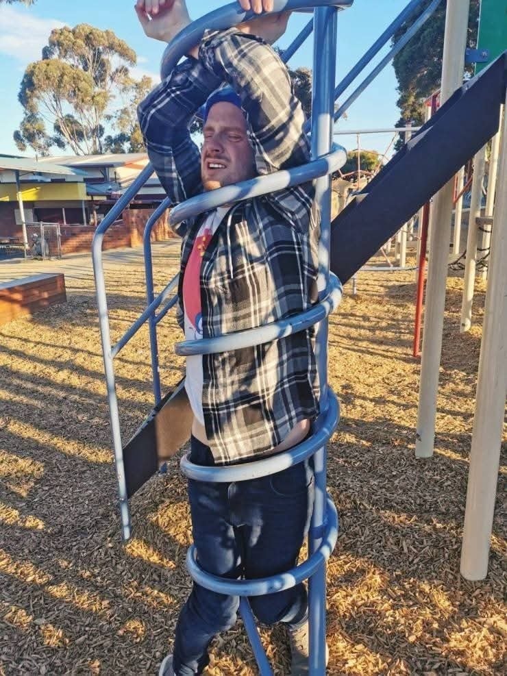 Muž uviazol v špirálovom preliezačke na ihrisku, usmievajúc sa napriek svojej situácii.